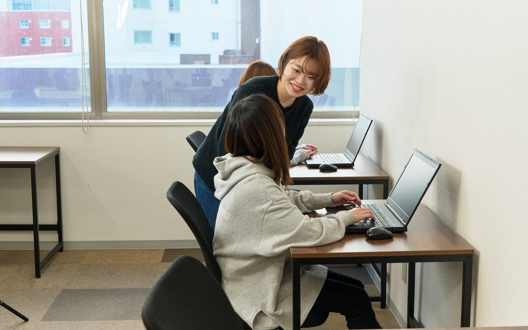 ノートパソコンで作業している人に、職員が横から声をかけている様子